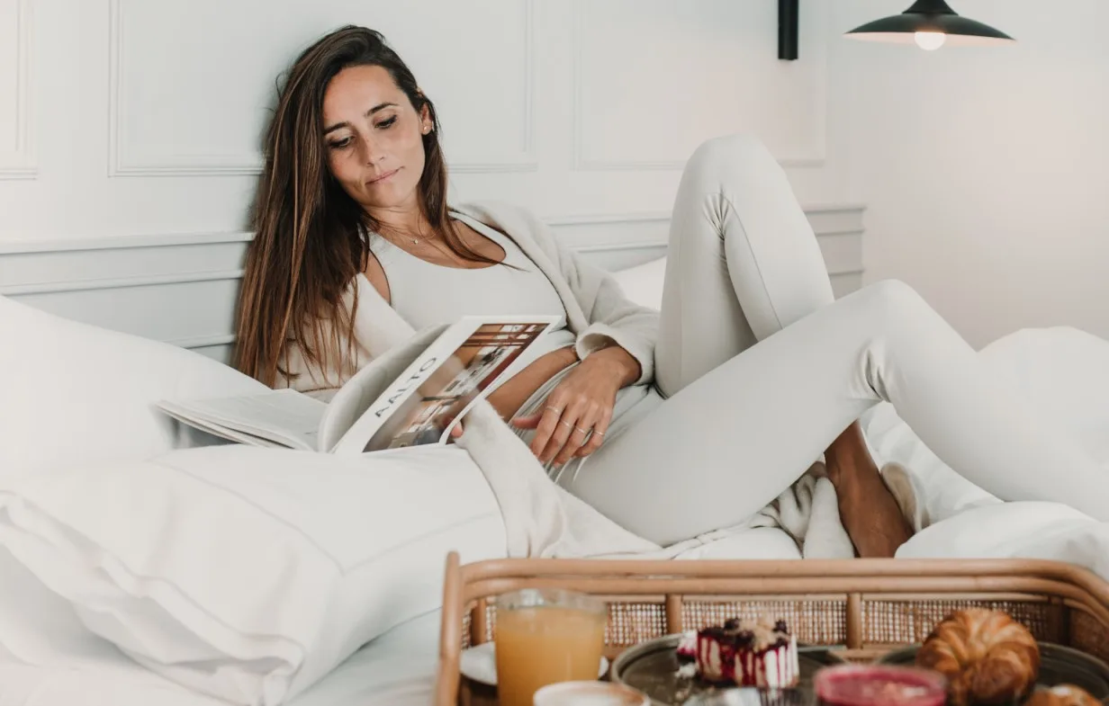 Representative hotel space: A woman relaxes on a white bed while looking through a magazine.