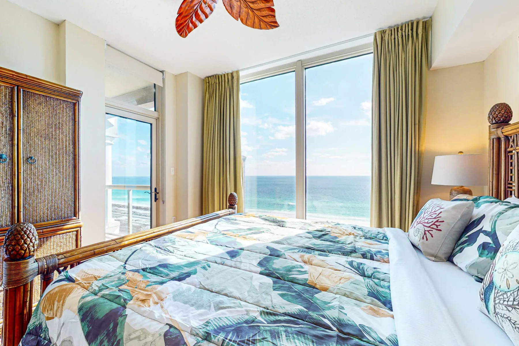 Un dormitorio con una colcha estampada junto a grandes ventanas con vistas al océano.