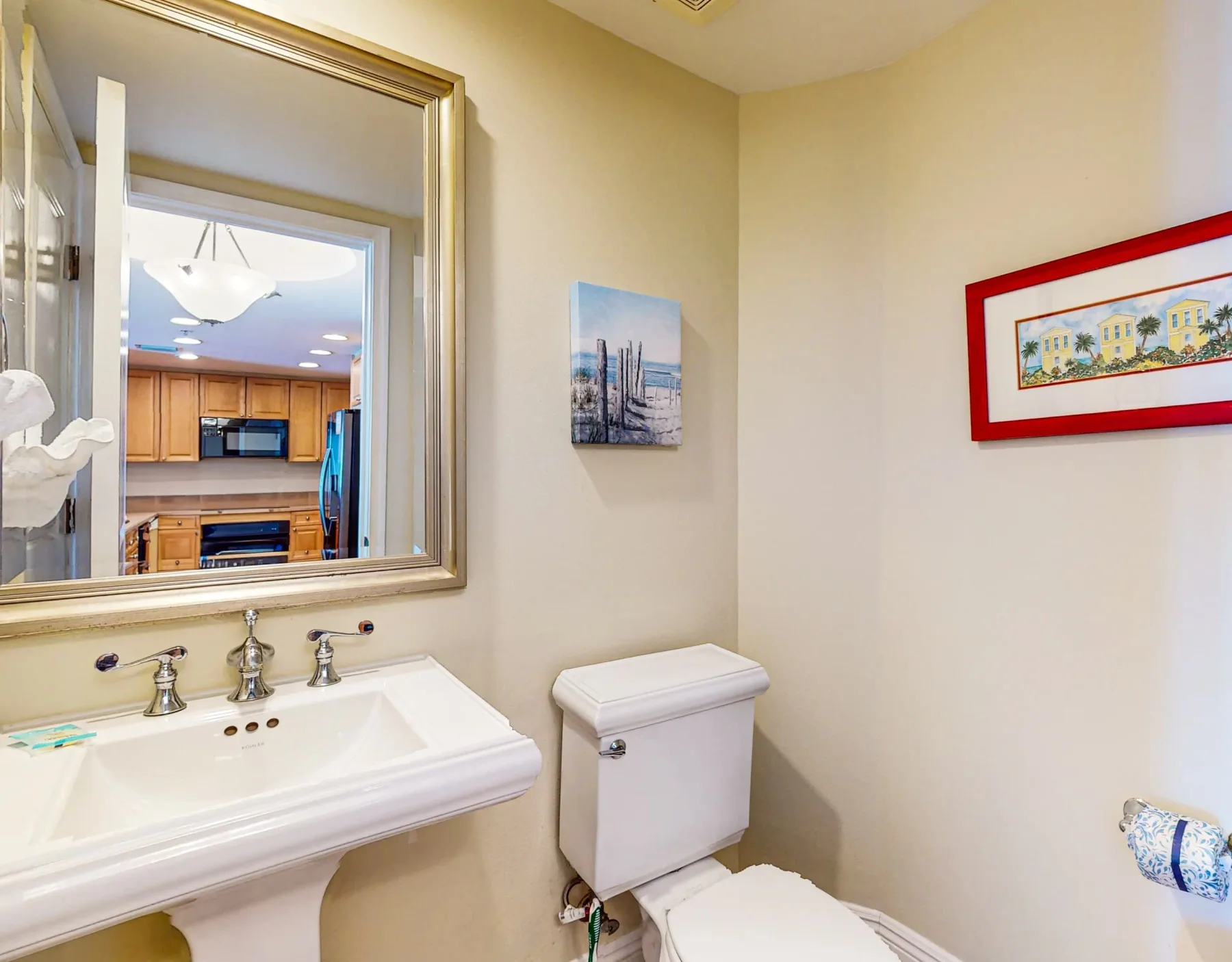 Un baño con lavabo, inodoro y un espejo que refleja la cocina.