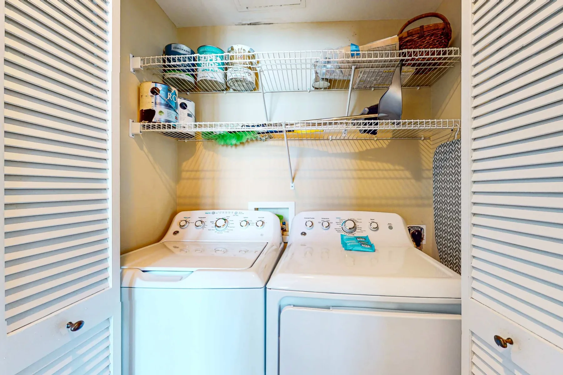 Un cuarto de lavandería con una lavadora y una secadora bajo estantes de alambre.