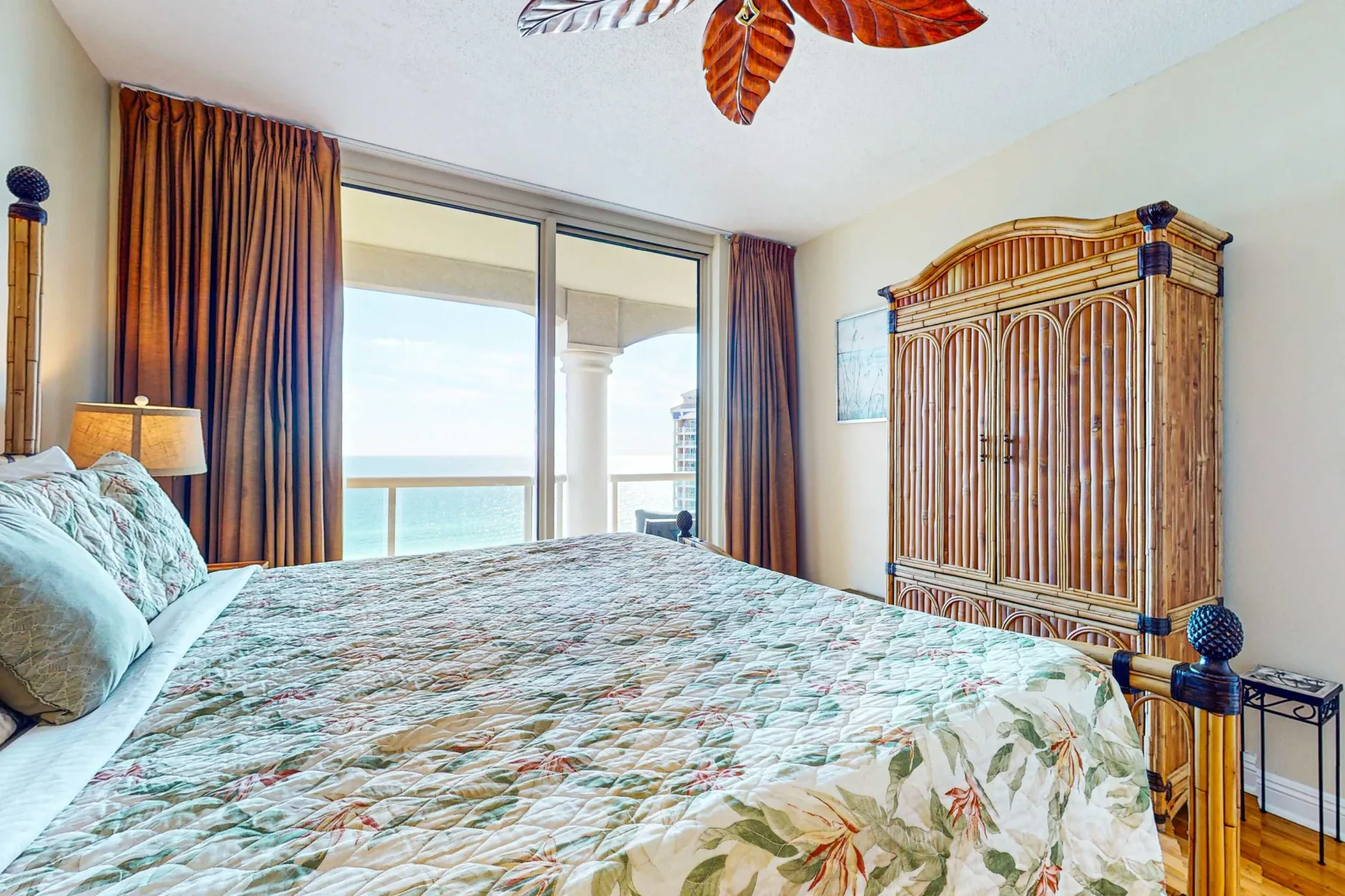 Un dormitorio con colcha floral, un armario alto de madera y puertas corredizas de vidrio.