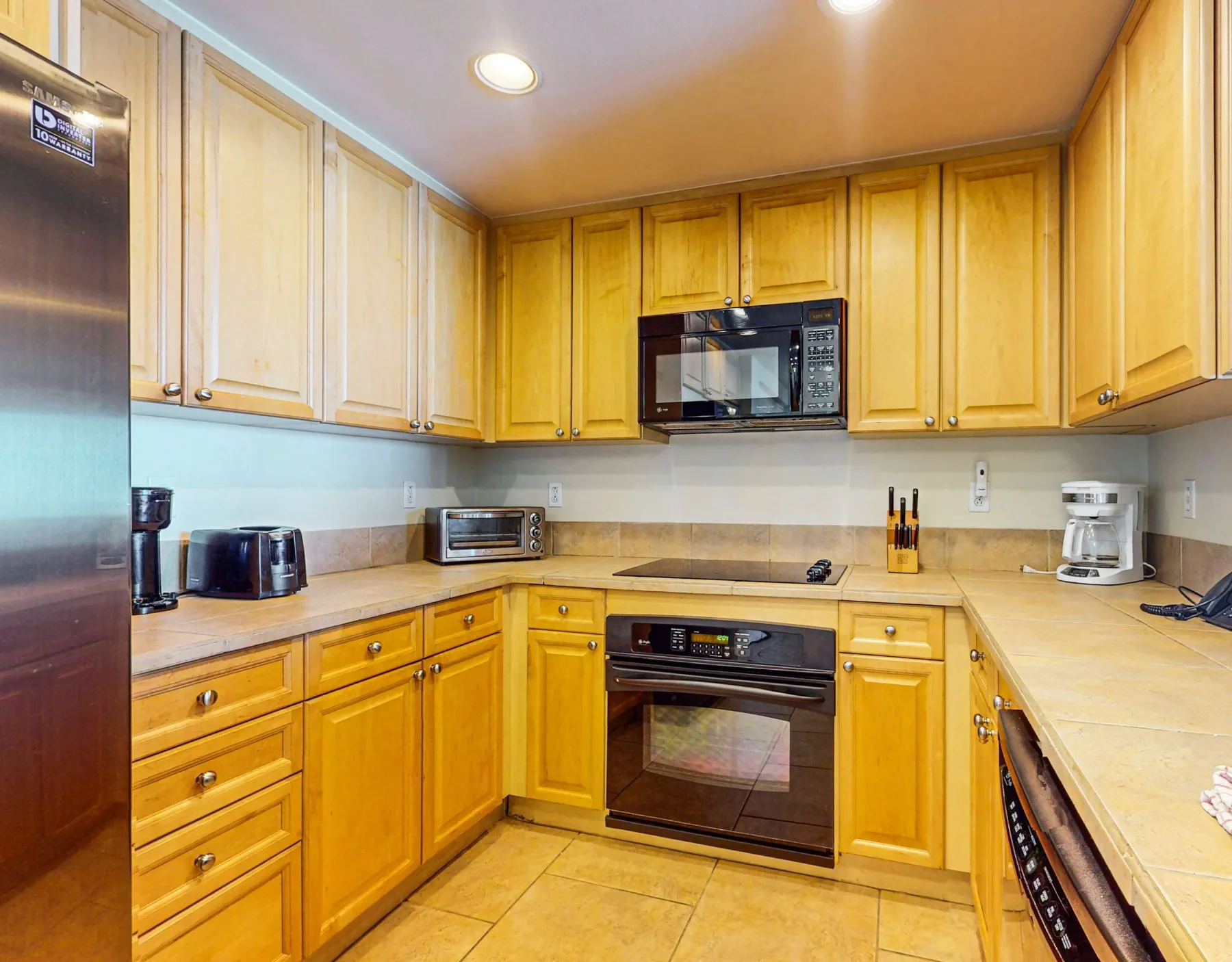 Una cocina luminosa con gabinetes de madera, electrodomésticos de acero inoxidable y piso de baldosas.