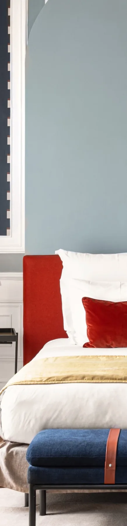 Espacio representativo del hotel: Dormitorio con ropa de cama blanca, cabecero rojo y un banco azul.
