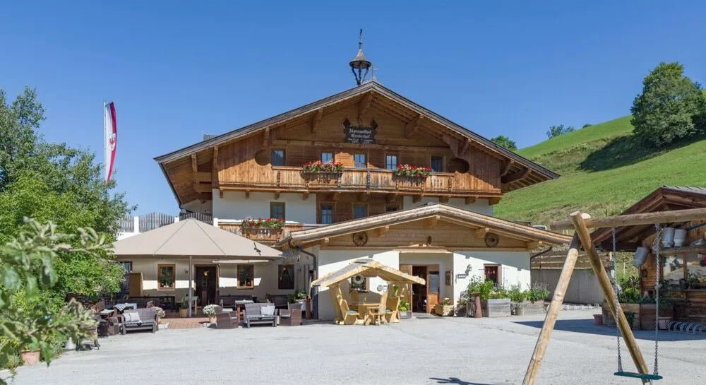 Espacio representativo del hotel: Un edificio de estilo chalet con balcones de madera junto a una zona pavimentada con asientos al aire libre.