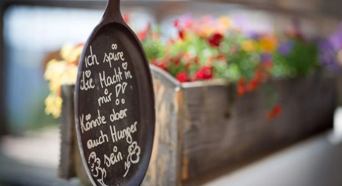 Espacio representativo del hotel: Una cuchara decorativa de madera con letras escritas a mano aparece frente a flores de colores.