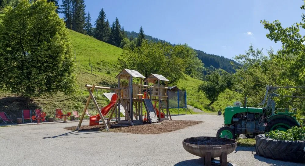 Espacio representativo del hotel: Un parque infantil al aire libre con juegos para trepar y un tractor junto a una ladera verde.