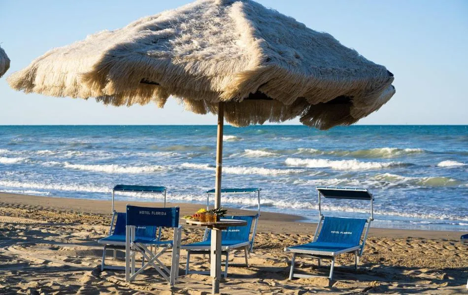 Espacio representativo del hotel: Una sombrilla de paja da sombra a asientos azules junto al mar.