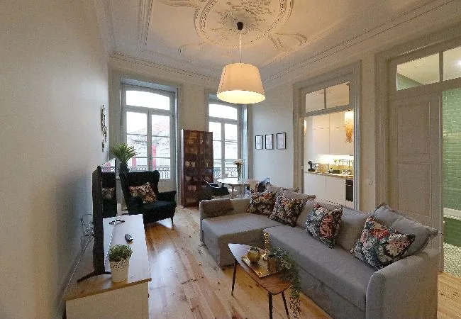 Una sala de estar con asientos, una mesa de centro y ventanas altas.