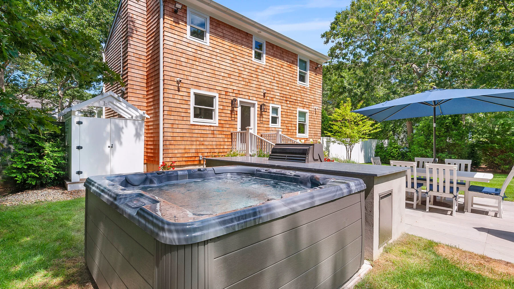 Una bañera de hidromasaje está junto a un patio con asientos al aire libre y una sombrilla azul.