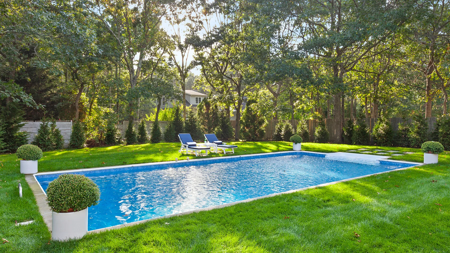 Una piscina está en un jardín con césped, rodeada de árboles.