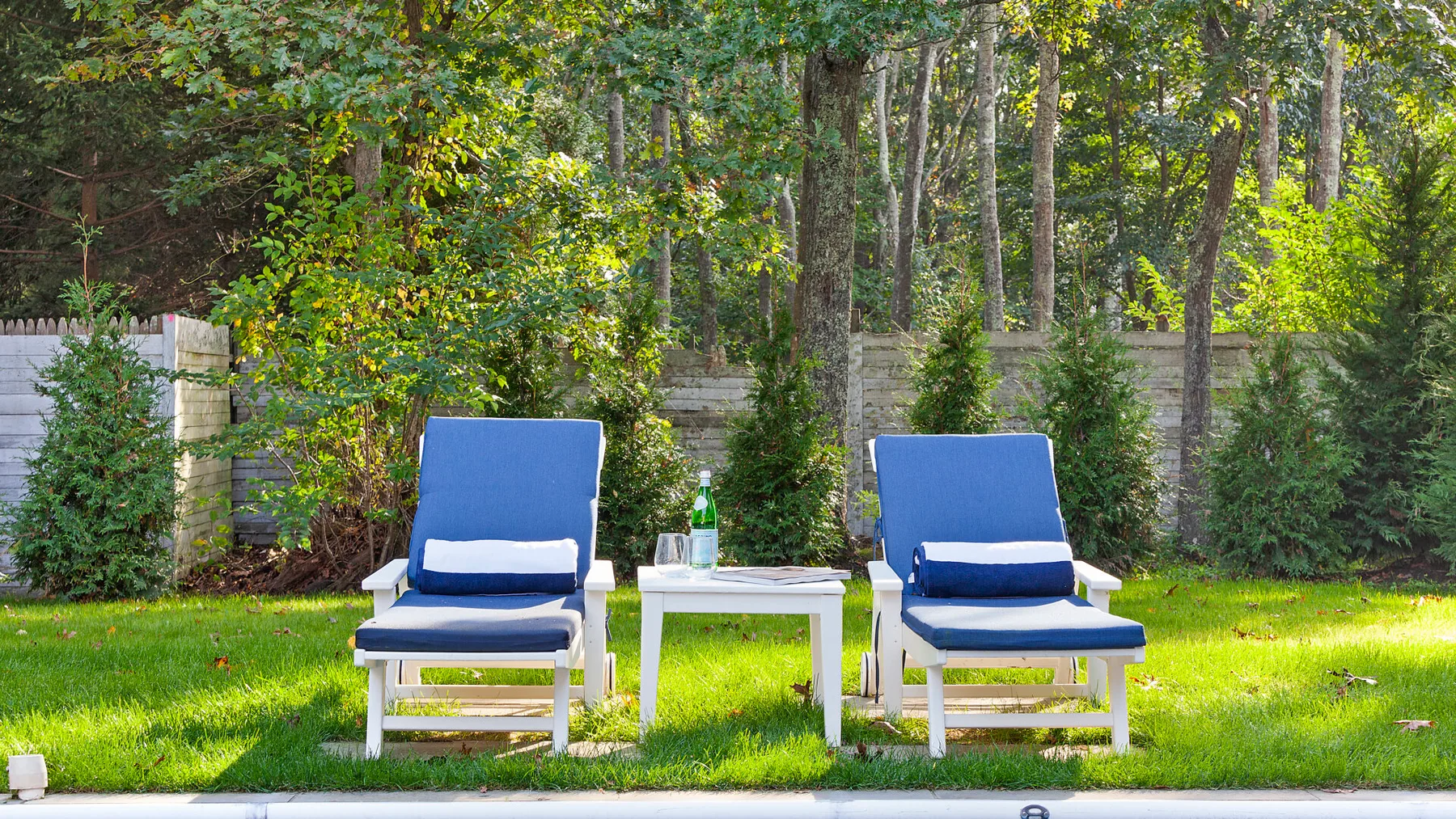 Una zona de estar al aire libre con dos sillones azules junto a una mesa pequeña.