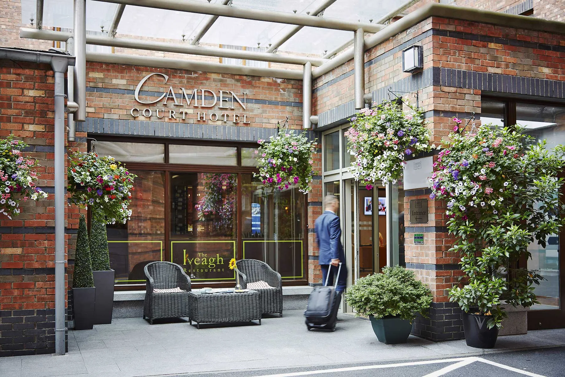 Representative hotel space: A brick hotel entrance sits beneath a glass canopy, with potted flowers nearby.