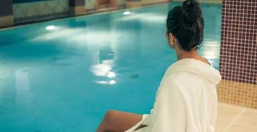 Representative hotel space: A person sits beside an indoor swimming pool with tiled edges.