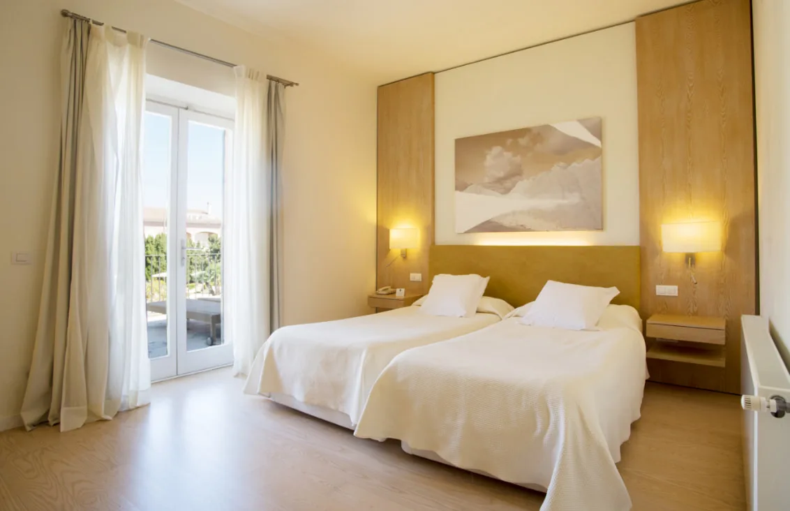 Representative hotel space: A bright bedroom with two beds and a glass door opening onto a balcony.