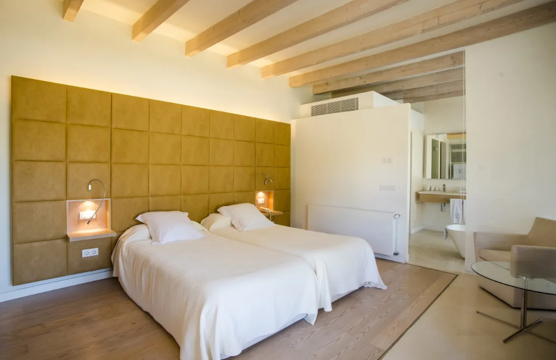 Representative hotel space: A bedroom with two beds, a padded headboard, and exposed ceiling beams.