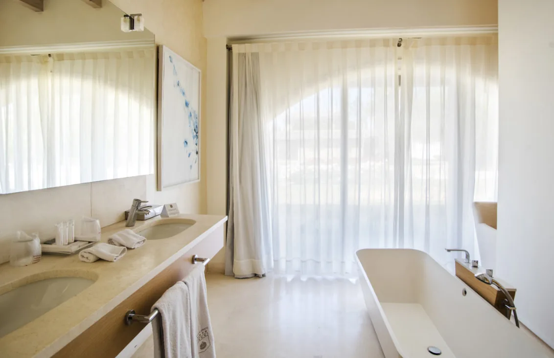 Representative hotel space: A bright bathroom with a bathtub and a vanity beneath large windows.