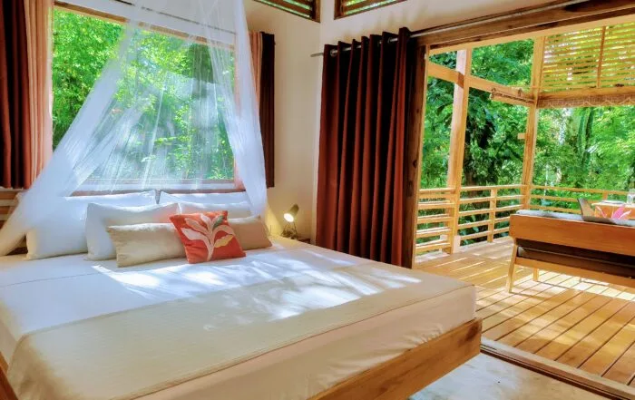 Espacio representativo del hotel: Un dormitorio con una cama junto a un balcón de madera con vistas a la vegetación.