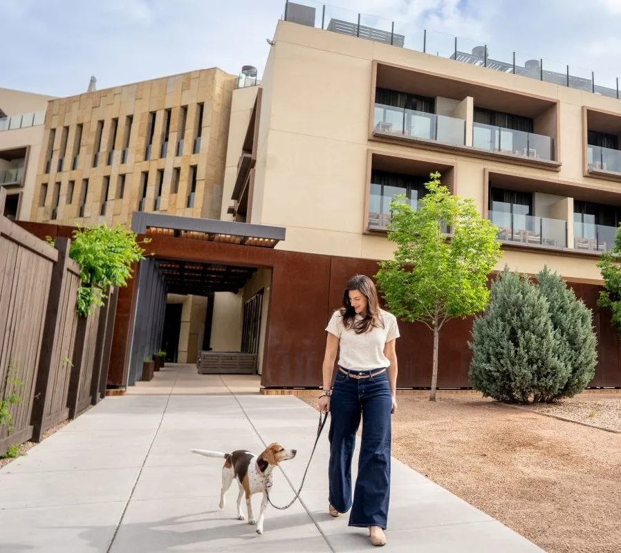 Representative hotel space: A woman walks a dog along a paved path outside a modern building.