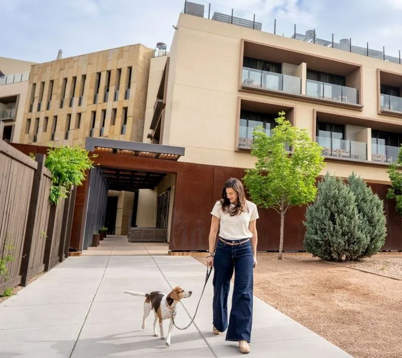 Representative hotel space: A woman walks a dog along the sidewalk outside a modern building.