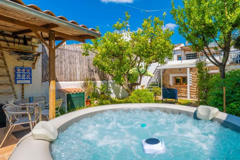 An outdoor hot tub sits beside a covered patio and leafy trees.
