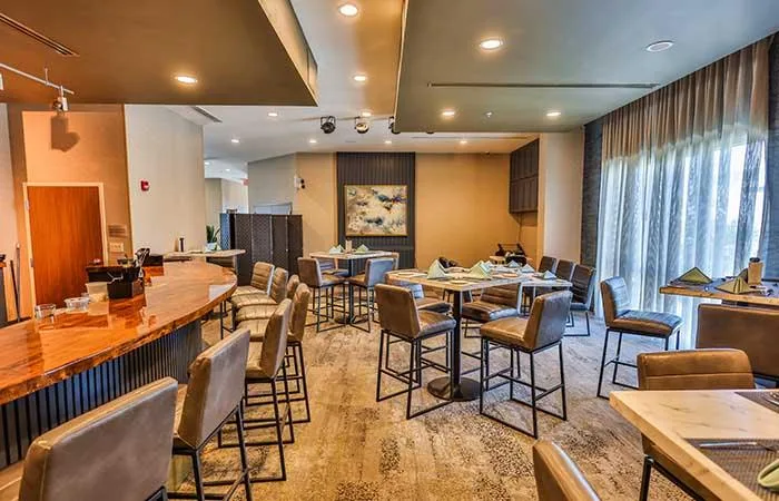 Espacio representativo del hotel: Comedor con asientos de barra y mesas junto a grandes ventanas con cortinas.