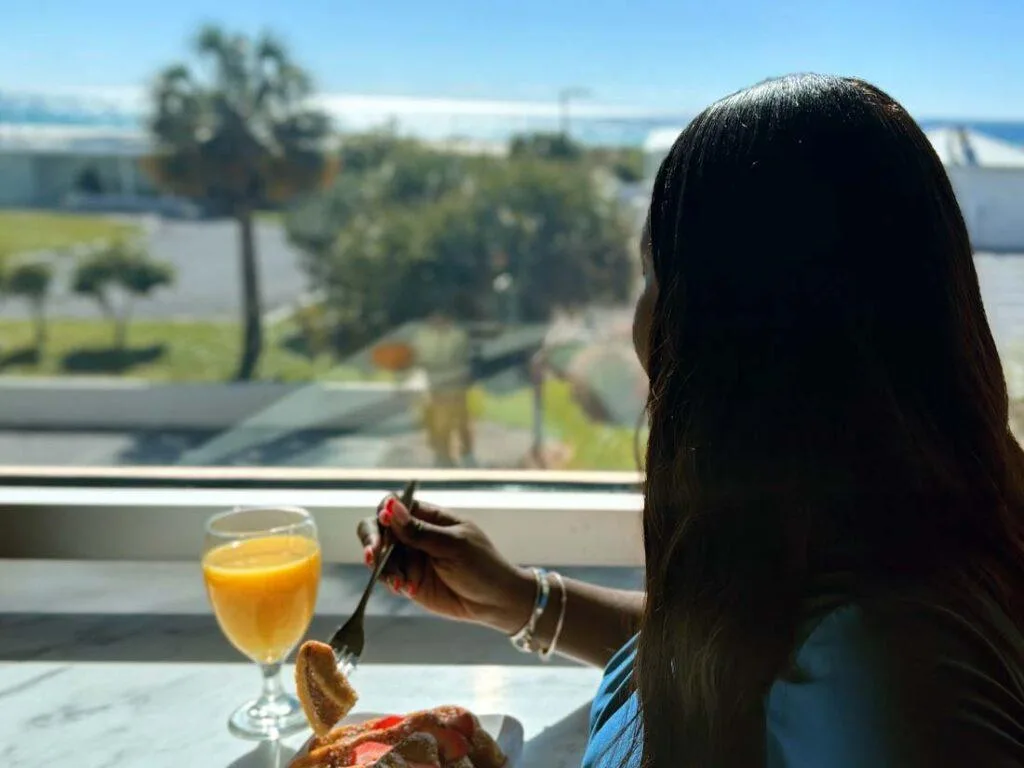 Espacio representativo del hotel: Una mujer está sentada junto a una ventana con un vaso de zumo de naranja.