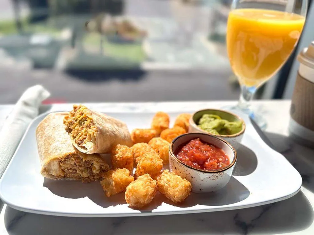 Espacio representativo del hotel: Un plato de desayuno con un wrap relleno, papas fritas, salsa y jugo de naranja.