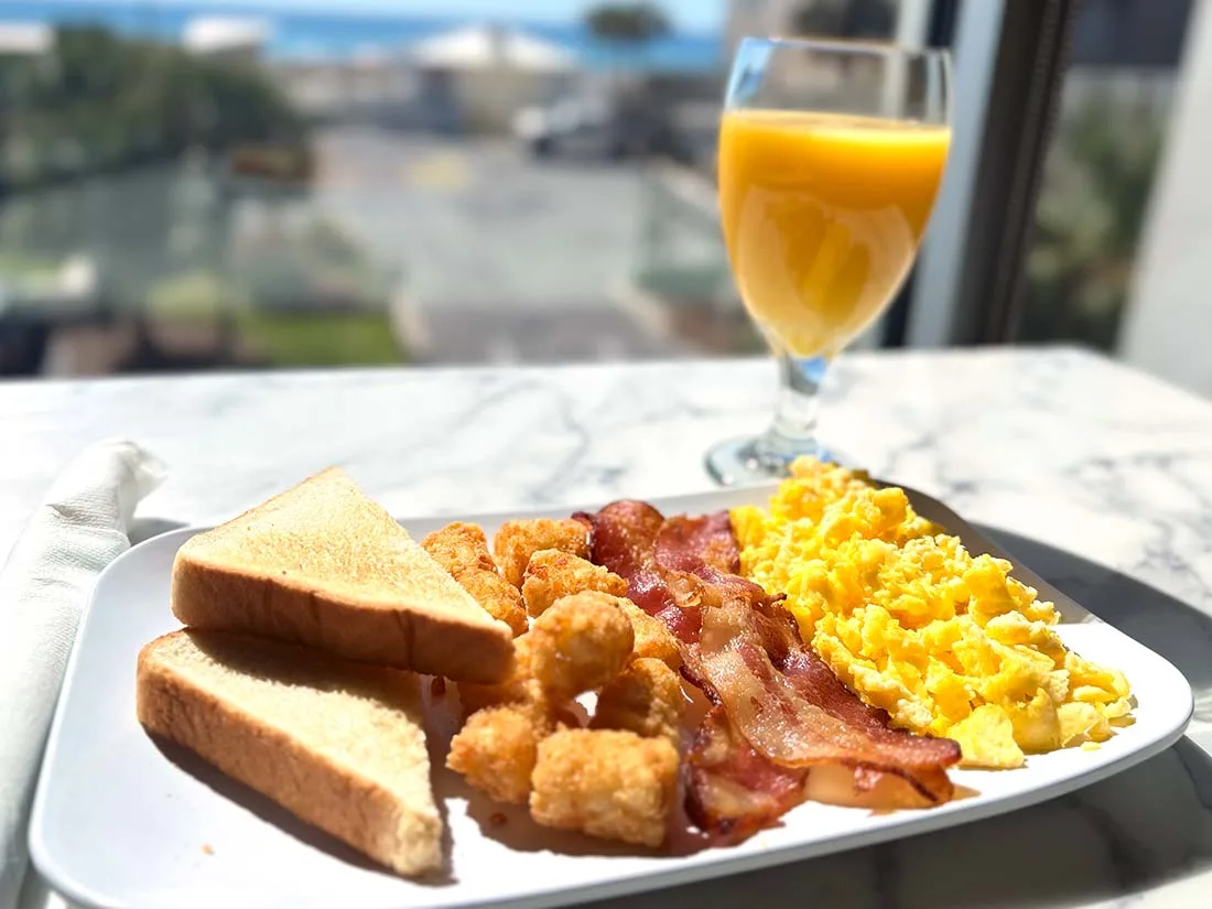 Espacio representativo del hotel: Un plato de desayuno con huevos, tostadas, tocino y jugo de naranja junto a una ventana.
