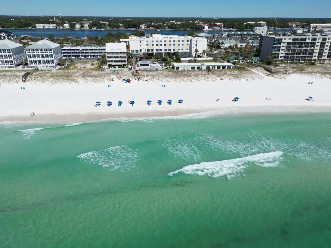 Espacio representativo del hotel: Vista aérea de una playa de arena y aguas turquesas junto a edificios frente al mar.