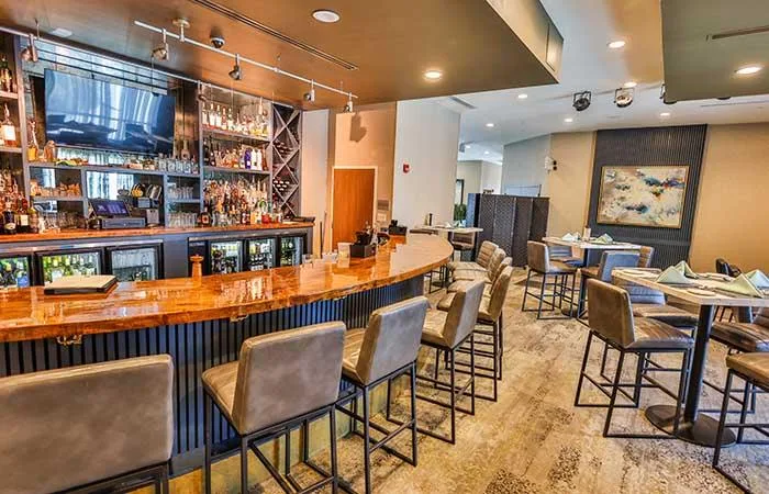 Espacio representativo del hotel: Un bar con una barra curva y asientos, junto a mesas dispuestas en el comedor.
