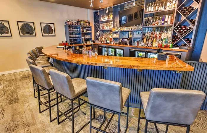 Espacio representativo del hotel: Una barra con asientos frente a estantes con botellas.