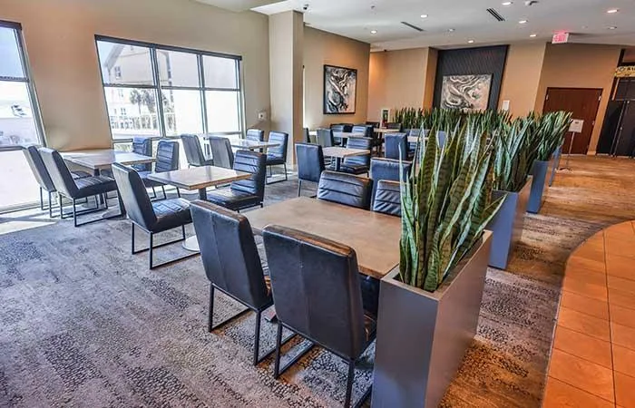 Espacio representativo del hotel: Un salón de hotel con asientos alrededor de mesas y plantas altas.