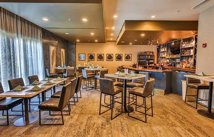 Espacio representativo del hotel: Un comedor con mesas y asientos frente a una barra con botellas.