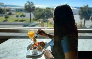 Espacio representativo del hotel: Una persona está junto a una ventana con el desayuno y vistas al paisaje.