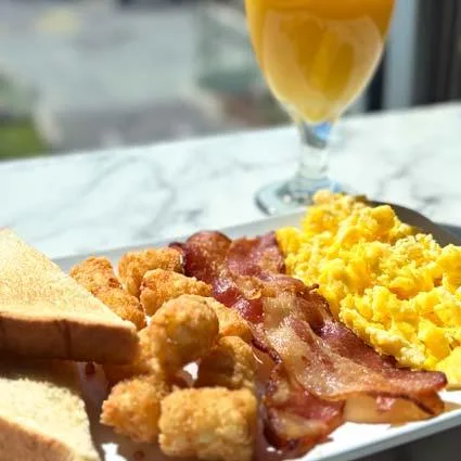 Espacio representativo del hotel: Un plato de desayuno con huevos, tocino, tostadas y un vaso de jugo de naranja.