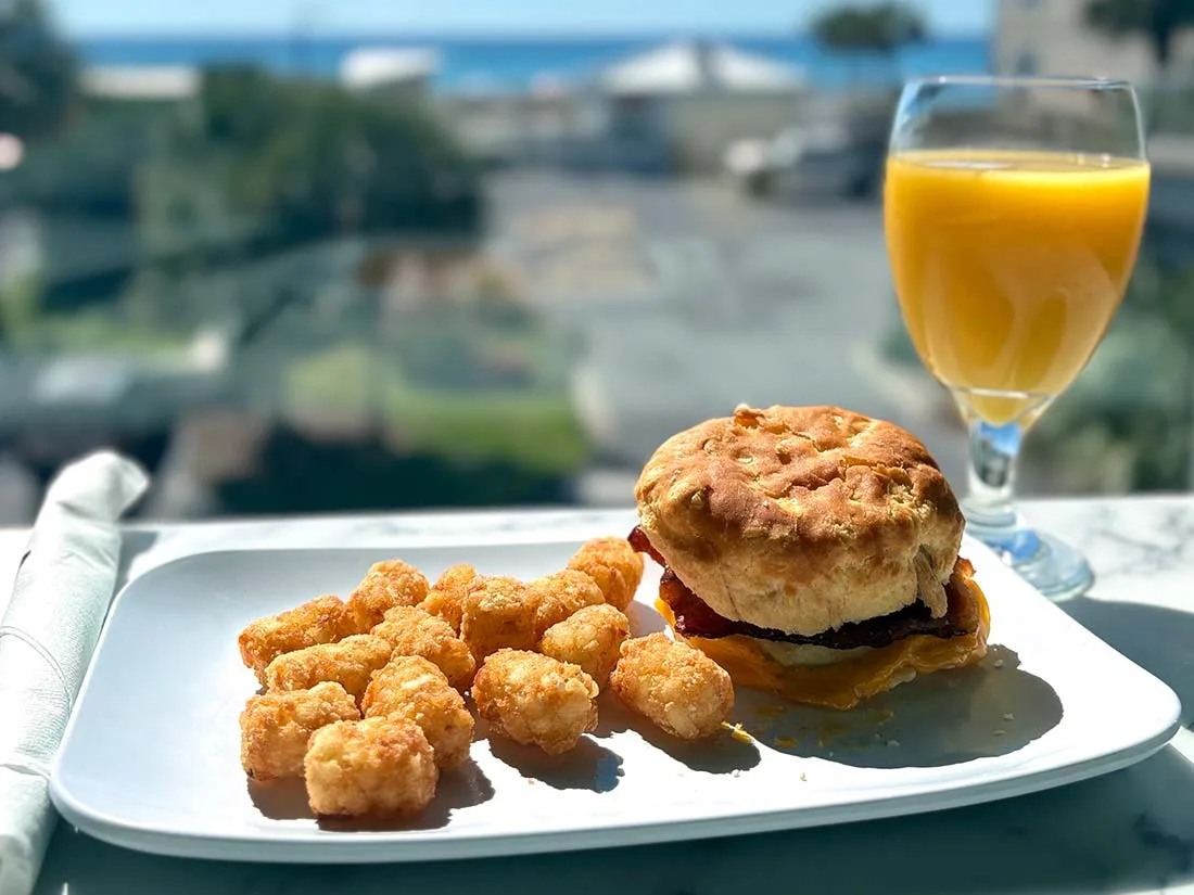 Espacio representativo del hotel: Un plato de desayuno con un sándwich, bocados fritos y un vaso de jugo de naranja.