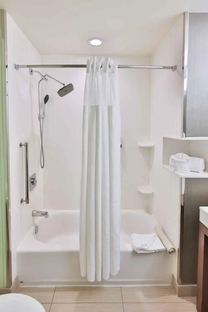 Espacio representativo del hotel: Zona de ducha de un baño con cortina y barras de apoyo.