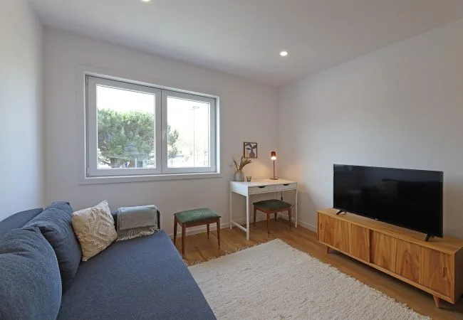 Una sala luminosa con asientos azules, un televisor y una ventana.