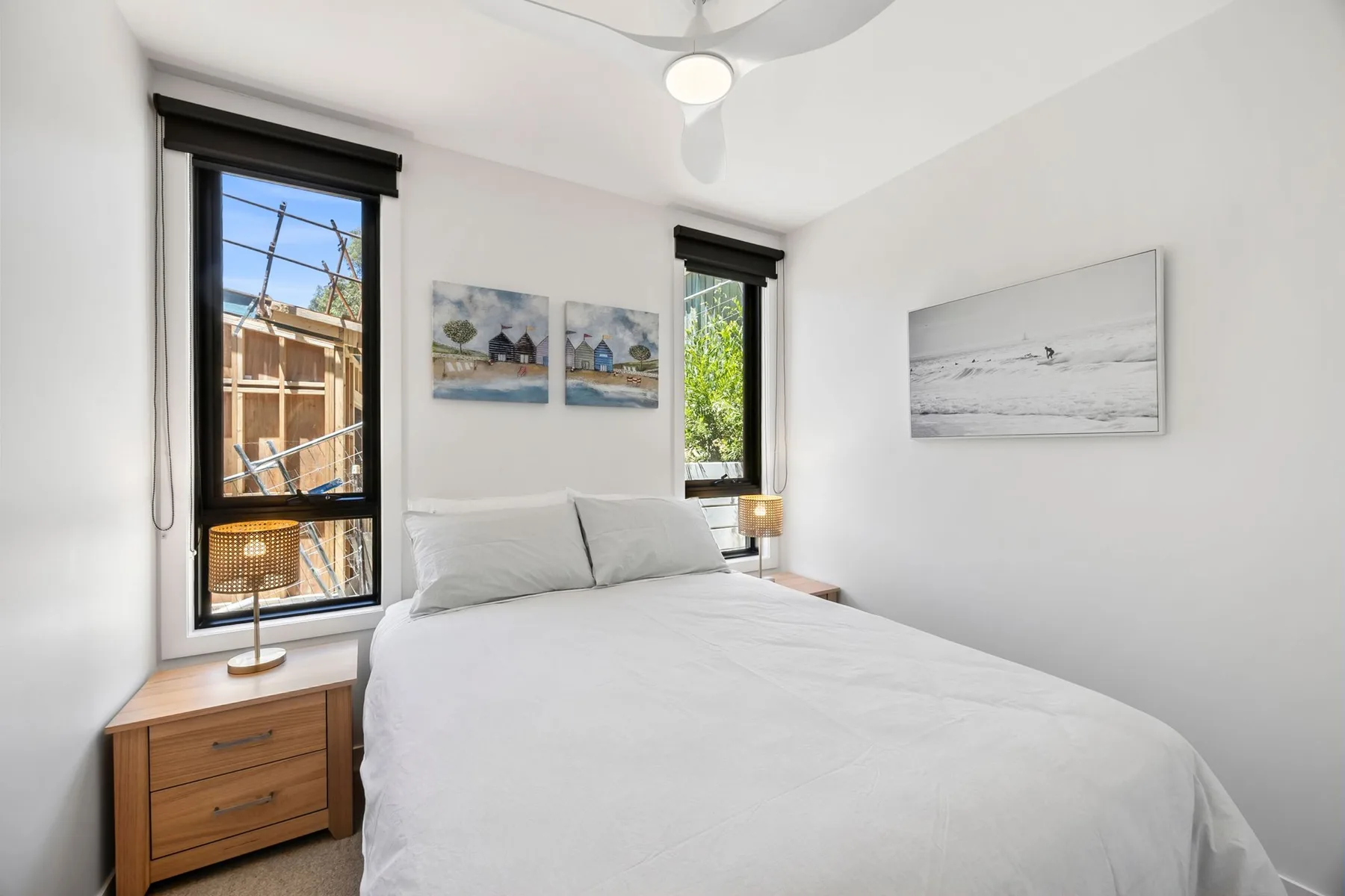 Un dormitorio luminoso con una cama bien tendida y cuadros en las paredes.
