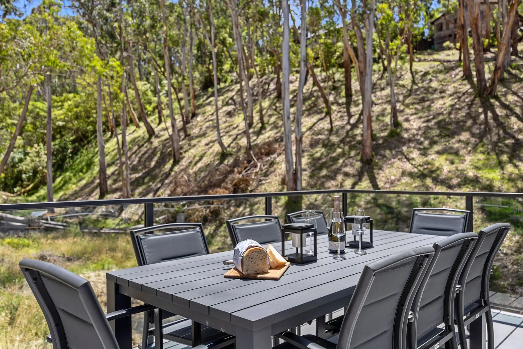 Una mesa de comedor al aire libre y asientos dan a una ladera arbolada.