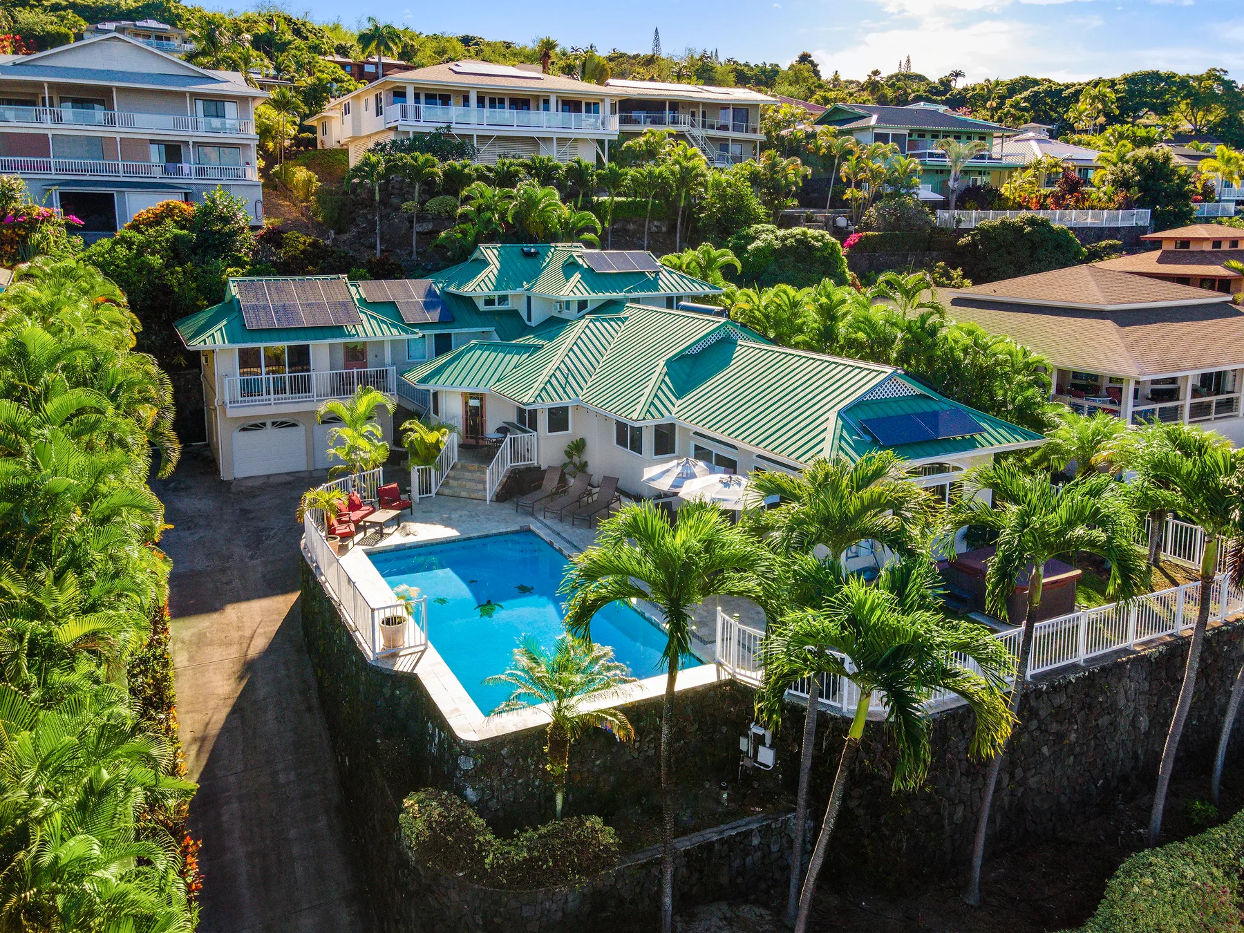 A tropical residential property with green roofs, lush landscaping, and a swimming pool.