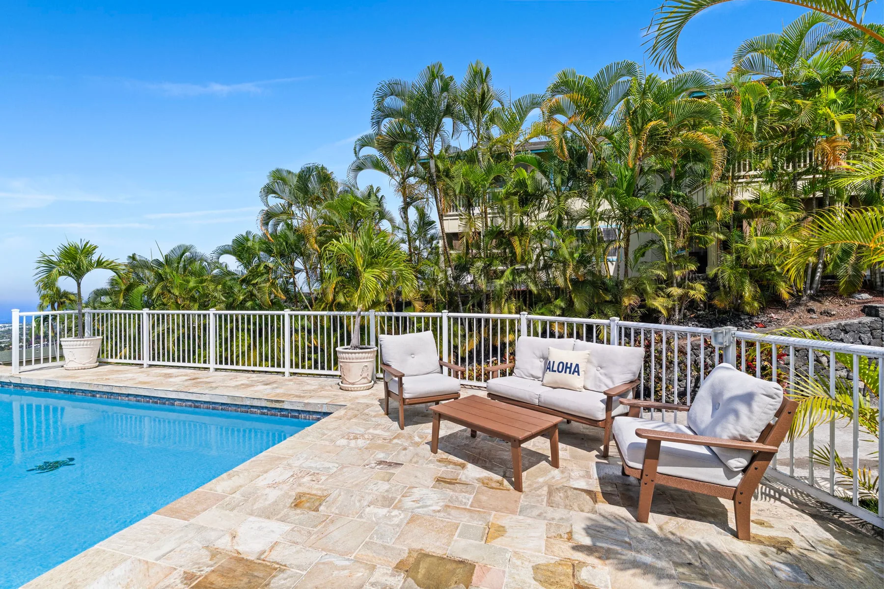A poolside patio with outdoor seating, tropical plants, and a white railing.