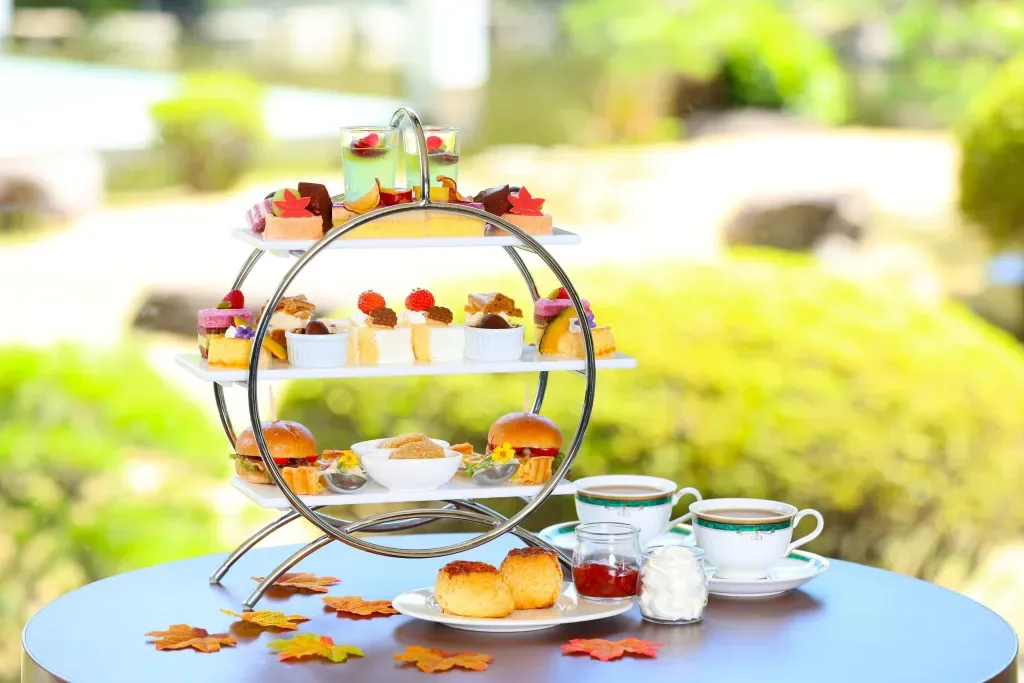 Espacio representativo del hotel: Un soporte de varios niveles muestra pequeños pasteles y té sobre una mesa al aire libre.