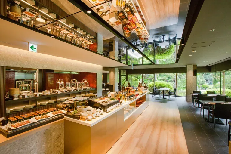 Espacio representativo del hotel: Comedor de hotel con un mostrador de bufé y mesas junto a grandes ventanas.