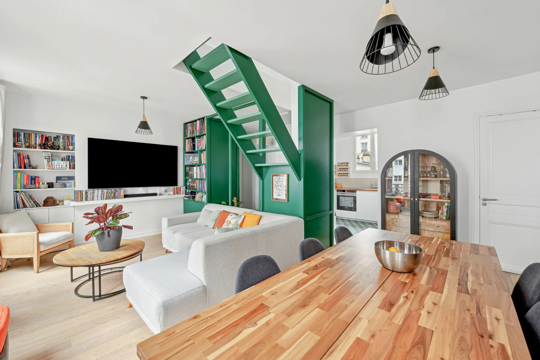 A bright open-plan living and dining area with a green staircase and wooden table.