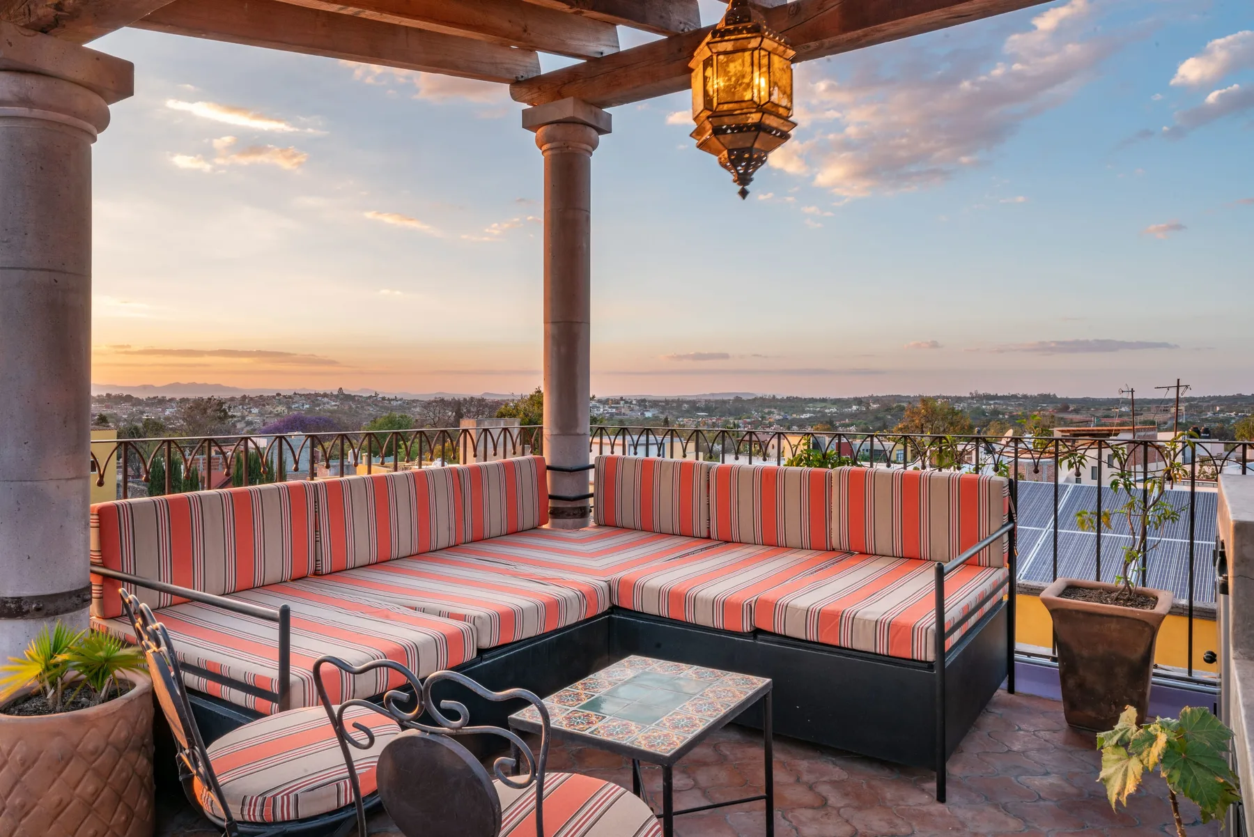 A covered outdoor seating area overlooks a town at sunset.