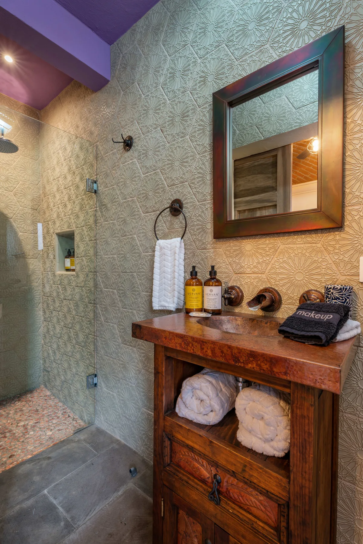 A tiled bathroom has a wooden vanity with a large mirror above it.