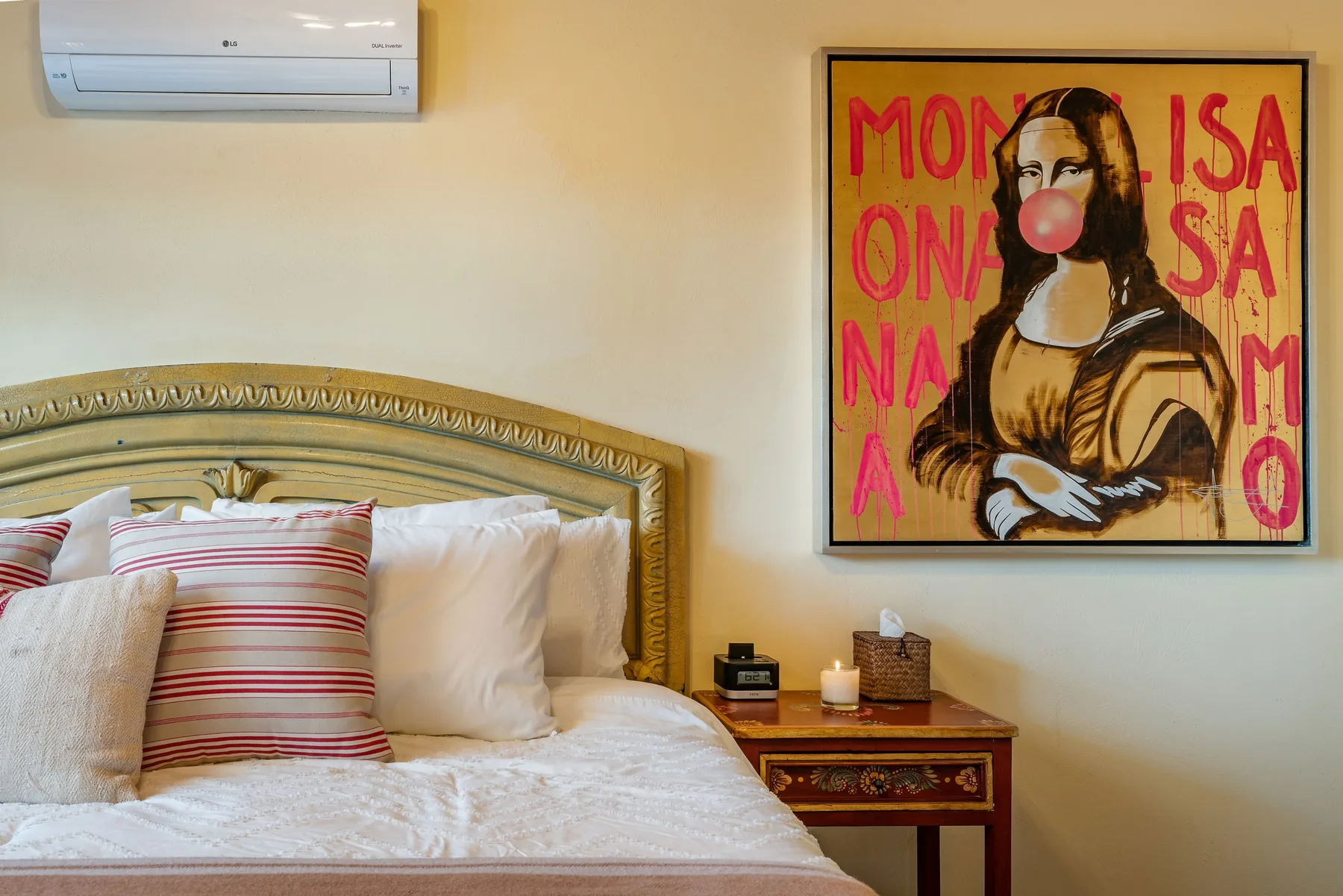 A bedroom with a bed, striped pillows, and framed artwork on the wall.