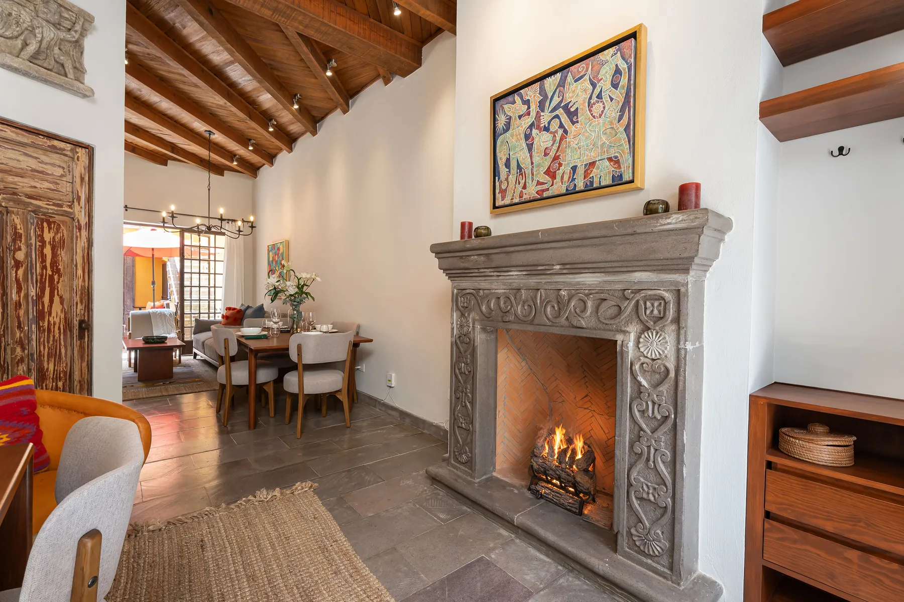 A dining and living area with a carved fireplace and a wooden ceiling.