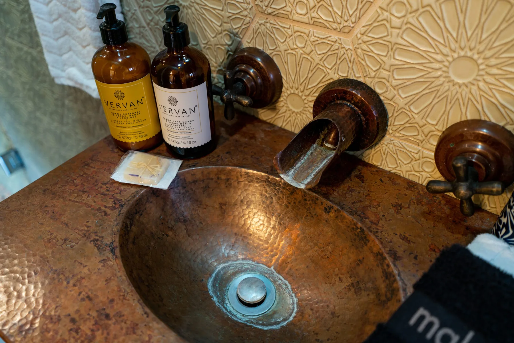 A stone vessel sink sits beneath a wall-mounted faucet against patterned tile.